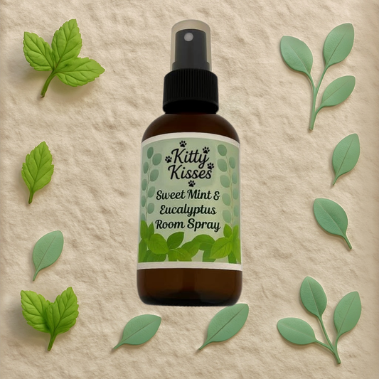 Bottle of Kitty Kisses Sweet Mint & Eucalyptus Room Spray surrounded by green leaves on a beige background
